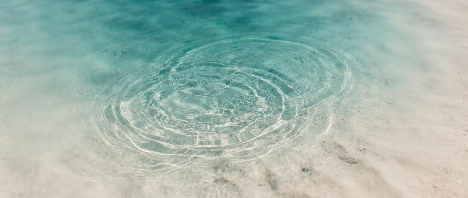 Ondas en la superficie de un agua clara sobre un fondo de arena